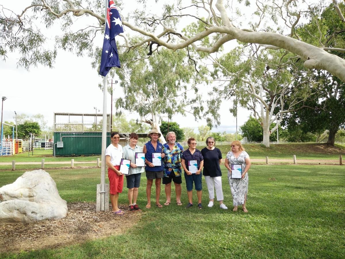 Seven award recipients standing under Australian flag