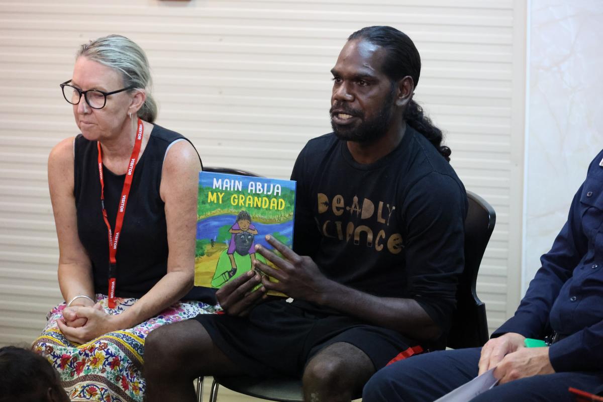 Two people sitting down. The man is holding a children's book