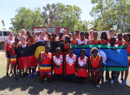 Two football teams holding flags for NAIDOC
