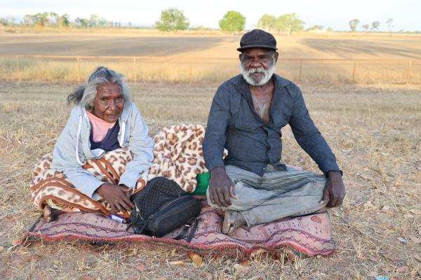 An elderly couple sitting on a rug outside