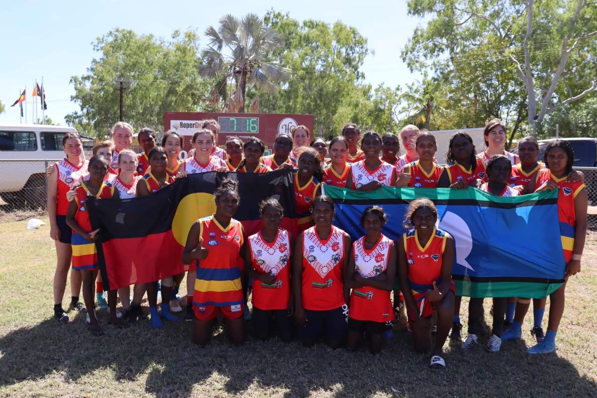 Two football teams holding flags for NAIDOC