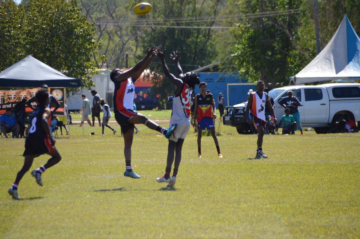 Two male football players jumping up to catch footy in day game