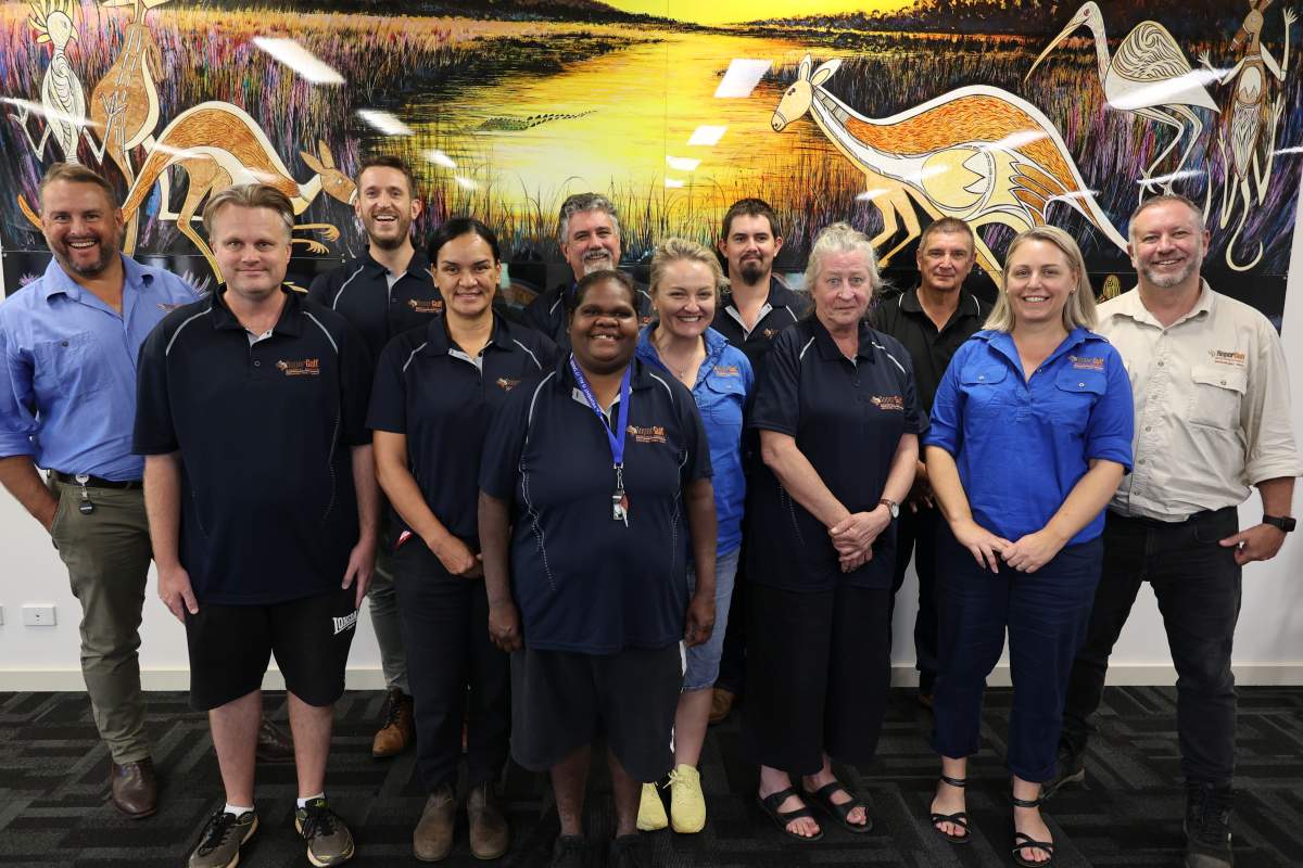 Group of staff standing in front of mural smiling at camera